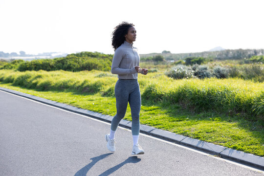 African American woman walking briskly on paved path wearing long sleeve zip top and white shoes