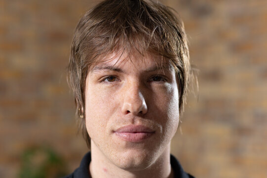 Man posing for portrait in studio with exposed brick wall, hoop earring, dark collar