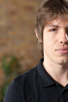 Man posing right side wearing black polo, showing small gold hoop earring, blurred plant