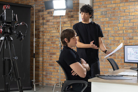 Diverse male coworkers discussing storyboard near camera in production studio, holding pages