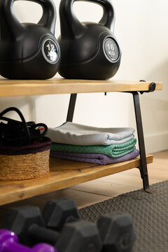 Kettlebells resting on top shelf in home workout corner, with folded mats, dumbbells