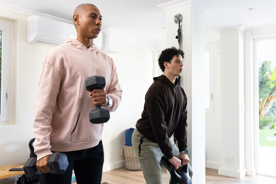 African American men wearing hoodies exercising in home gym holding hex dumbbells and kettlebell
