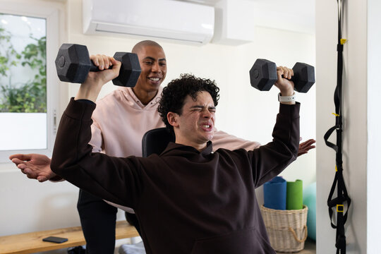 African American male trainer and client spotting client lifting dumbbells on bench at home gym