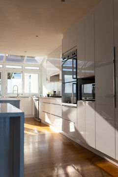 Wall of glossy white cabinets is featuring built-in ovens and microwave in bright modern kitchen