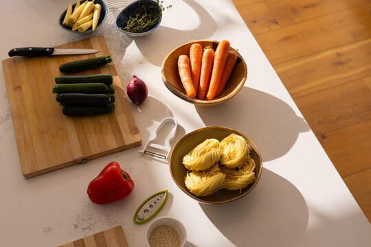 Wooden bowl holding carrots and ceramic bowl nesting pasta are basking in warm sun on countertop