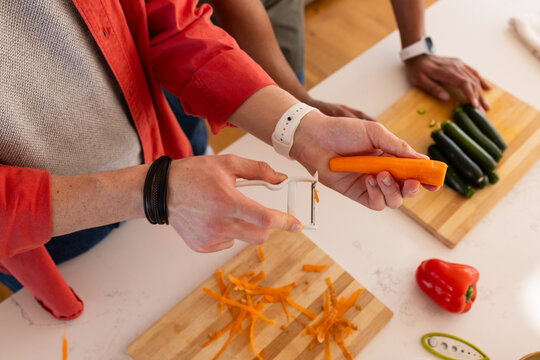 African men peeling carrot and arranging zucchini on white counter with Y style peeler and watches