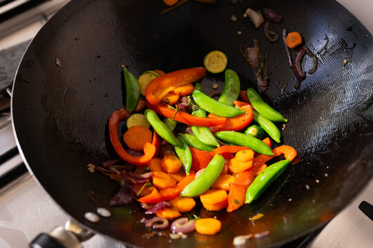 Carbon-steel wok cooking colorful vegetable stir-fry on gas stovetop, showing glossy browned bits