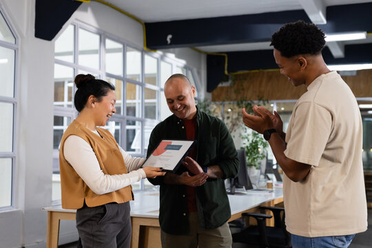 Diverse coworkers clapping and presenting framed certificate in modern office wearing work clothes