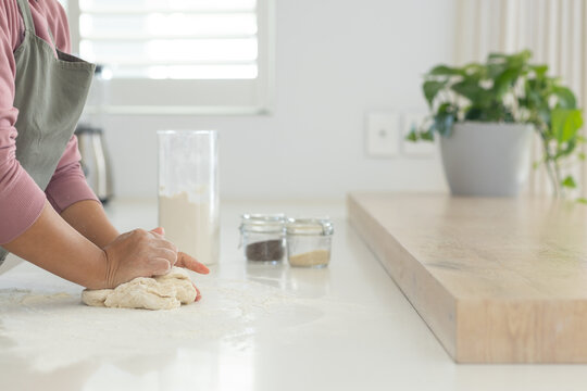 Asian woman kneading dough on flour-dusted countertop at home, wearing grey apron, copy space