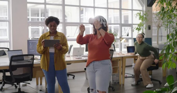 Female team watching woman wearing VR headset gesturing while starting demo with tablet in office