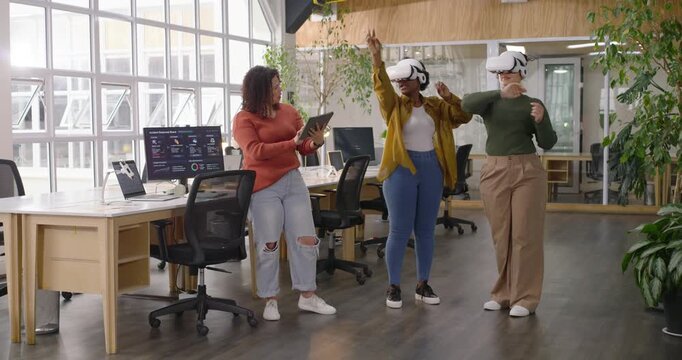 Diverse women coworkers in office coach holding tablet instructing donning VR headsets for training