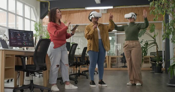 Female colleagues initiating tablet-driven VR demo in open-plan office, headset users gesturing