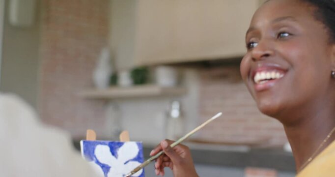 African American couple woman-yellow-top applying blue strokes on canvas at home after partner cue