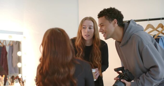 Diverse creative team directing and prepping seated model at studio vanity with DSLR and coffee