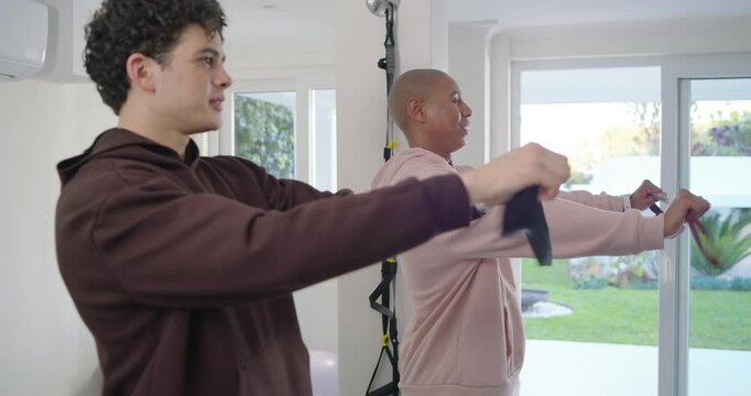 Two adult men in hoodies exchanging glances, pulling resistance bands at home for workout