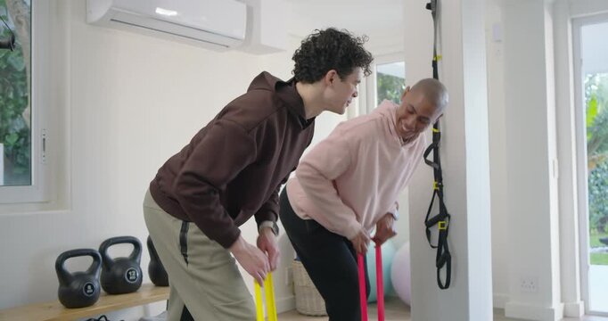 African American men anchoring looped bands at feet, doing hinged rows in home gym coaching form