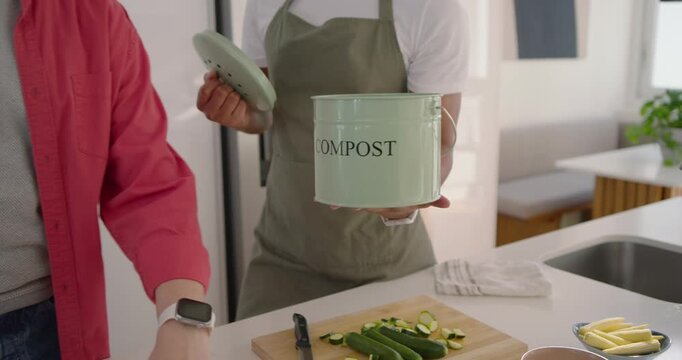 Diverse male pair, adult offering compost pail while teen peeling zucchini for compost in kitchen