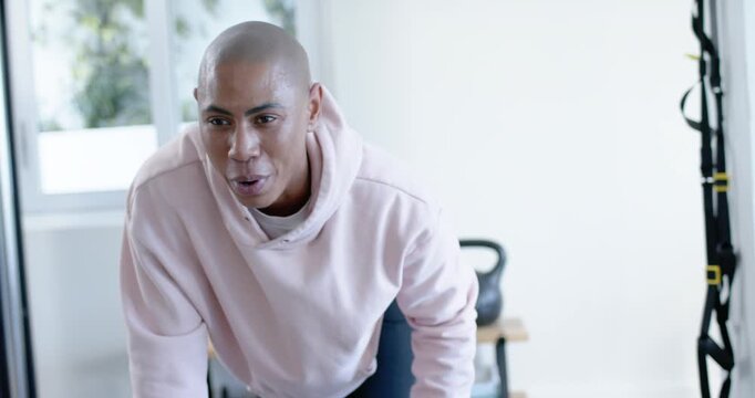 African male training pair, partner cueing trainer in pink hoodie pulling hex dumbbell at home gym