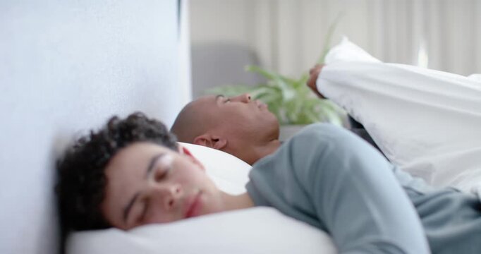African American men waking after pause in bed, older man lifting duvet, tucking for warmth