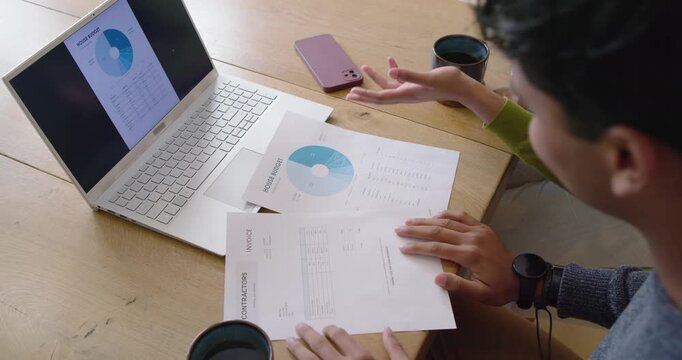 Diverse coworkers man reaching aligning laptop chart with bills on table checking totals