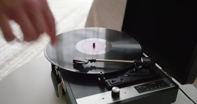 Person is placing vinyl on turntable by window, lowering tonearm and turning knob to play music