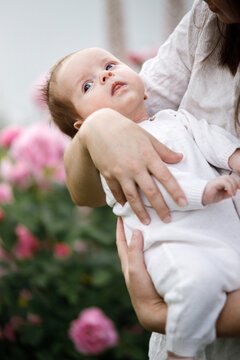 Cute newborn baby in mother hands close up among flowers in the garden. Love, care and family in countryside concept. Happy Mothers day! Adoption and maternity