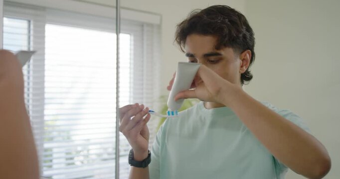 African American man squeezing paste onto brush brushing teeth at sink near mirror for dental care