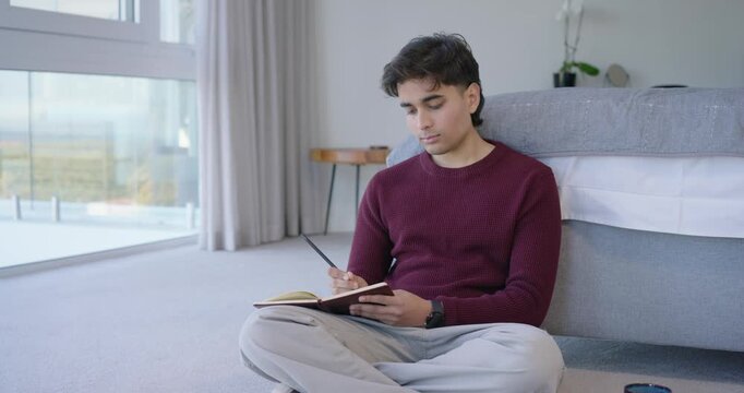 African-American man sitting on bedroom floor writing in notebook with pen view causing reflection