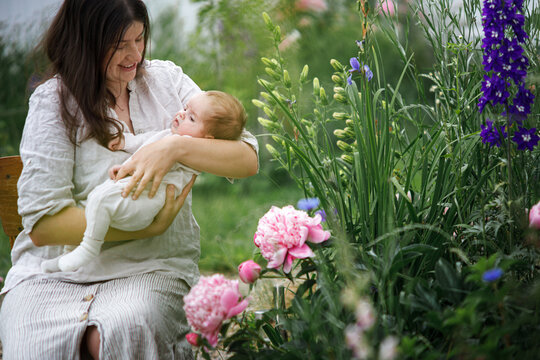 Mother hugging cute newborn baby among flowers in the garden. Love, care and family in countryside concept. Happy Mothers day! Adoption and maternity