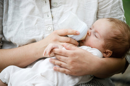 Mother feeding cute newborn baby with bottle close up in the garden. Love, care and family in countryside concept. Happy Mothers day! Adoption and maternity