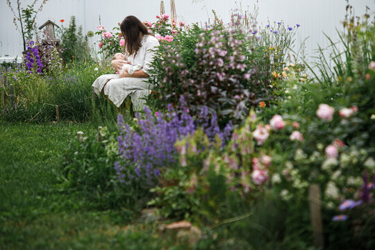 Mother hugging cute newborn baby among flowers in the garden. Love, care and family in countryside concept. Happy Mothers day! Adoption and maternity