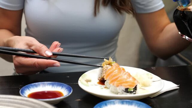 Close Up of Woman Pouring Soy Sauce from Small Bottle onto Fresh Salmon Sushi Roll Holding Chopsticks Asian Restaurant Dining Food Concept Outdoors