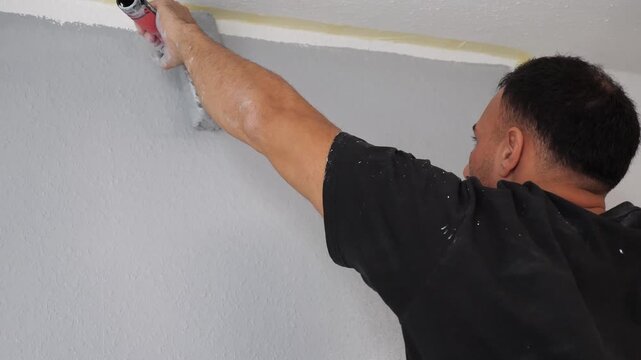 Professional Painter Rolling Grey Paint on Wall Below Masking Tape Line Home Renovation Precision Interior Decorating DIY Improvement Concept Indoors
