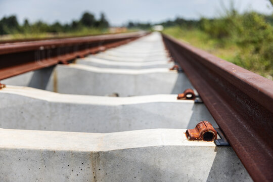 steel railway rails resting on concrete sleepers before fastening clips are installed. Unfinished railway track extending into the distance at an outdoor construction site.
