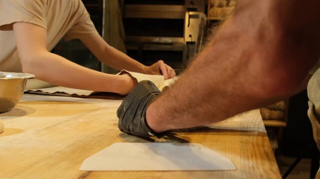 Baker in black gloves shapes soft dough on floured wooden table. Skilled worker presses pastry tapping surface to form even compact piece