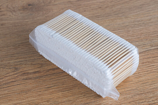 Pack of wooden cotton swabs in transparent plastic wrap on wooden table. Eco friendly hygienic cotton buds, personal care, medical supplies, cosmetic applicators and ear cleaning concept.