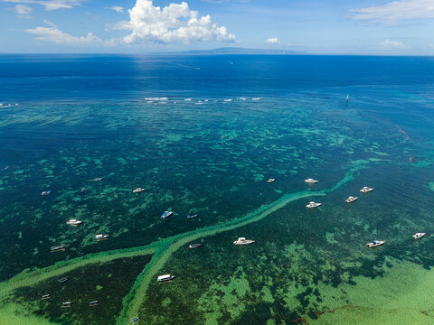 Aerial view of tropical coast with shallow reef and turquoise sea, distant island silhouette on horizon under cumulus cloud, Indonesia