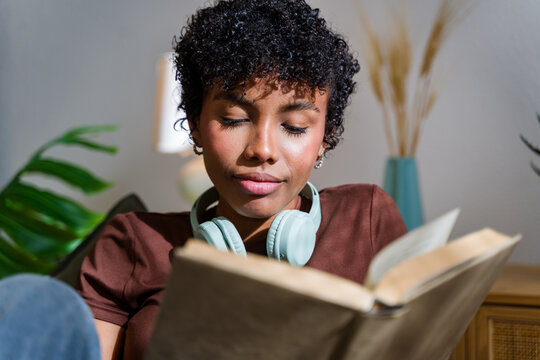 African American woman reading a book indoors wearing headphones