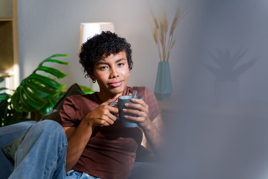 African American woman relaxing on sofa holding a cup indoors
