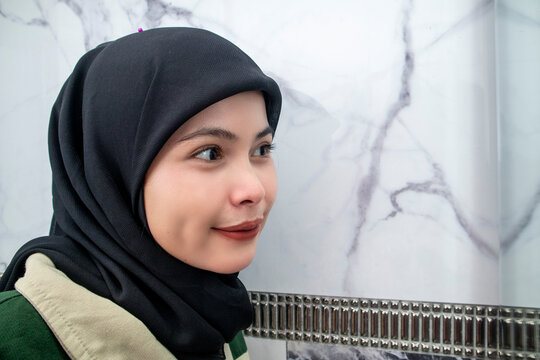Close-up three-quarter portrait of a smiling young Asian Muslim woman in a hijab with dimples indoors.