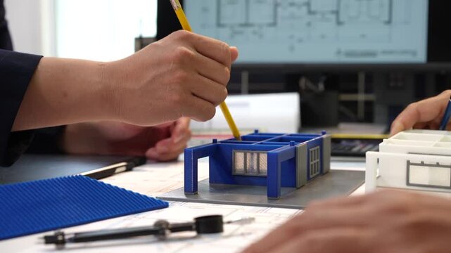 Architects work on a small building model with plans, ruler and pencil in a design studio.