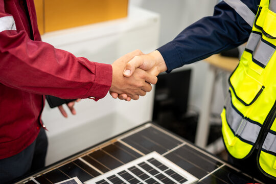 Close-up of a business handshake between a client and solar energy worker over photovoltaic panels, showing agreement on renewable power installation.