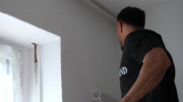 Professional Male Painter Painting Interior Wall White with Roller Tool in Modern Room Renovation Project DIY Home Improvement Concept Medium Shot