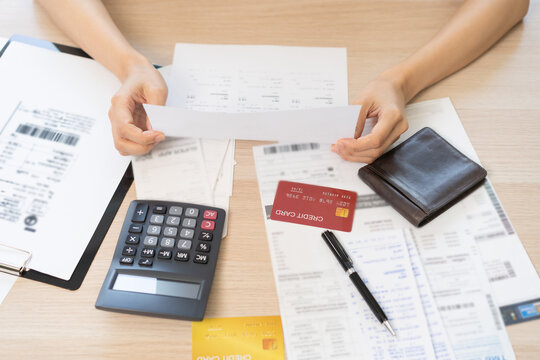 Debt and financial concept, stressed asian young woman have a headache while female calculate expenses, income and expenses, looking bills of credit card for payment or payday on table at home office.