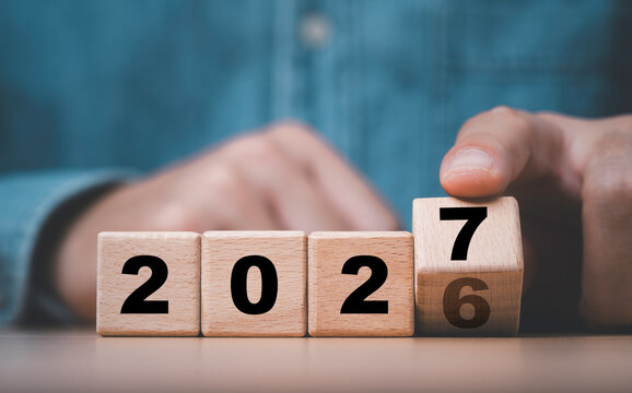 Hand turning wooden number blocks from 2026 to 2027 symbolizing New Year transition for fresh beginnings, business future planning goals and new opportunities for the coming year.