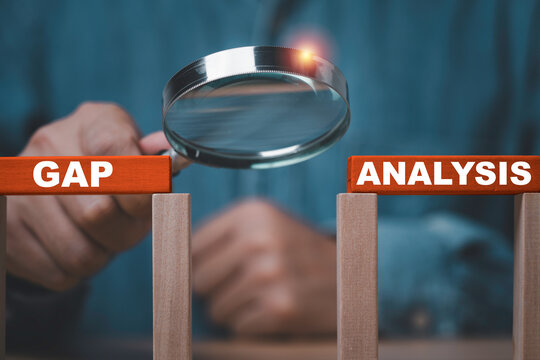 Business gap analysis concept with a person holding a magnifying glass over a gap between wooden blocks symbolize performance assessment of strategic planning, problem solving and improvement.