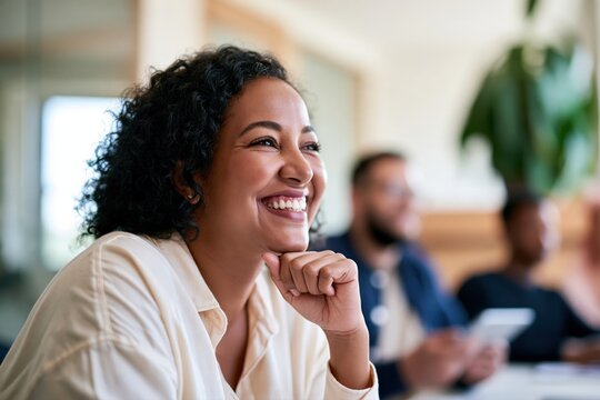 Happy colleague listening attentively during an office meeting; smiling businesswoman with curly hair in a friendly team environment