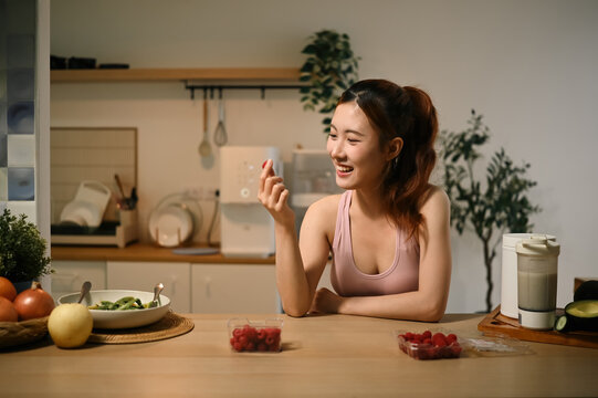 Young Asian Woman Enjoying Fresh Raspberries in Kitchen for Antioxidant Skin Nourishment and Anti Aging Benefits