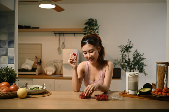 Young Asian Woman Enjoying Fresh Raspberries in Modern Kitchen for Healthy Skin and Anti Aging Benefits