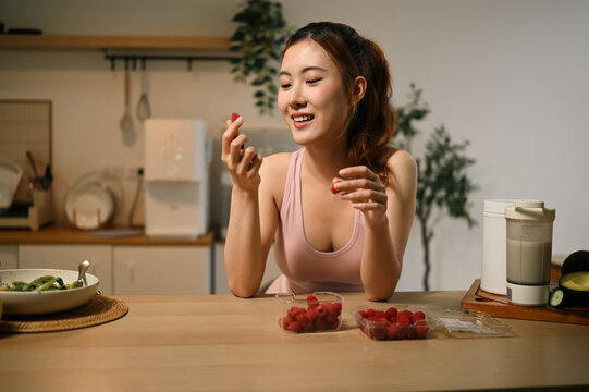 Young Asian Woman Enjoying Fresh Raspberries at Home Kitchen for Skin Nourishment and Antioxidant Benefits